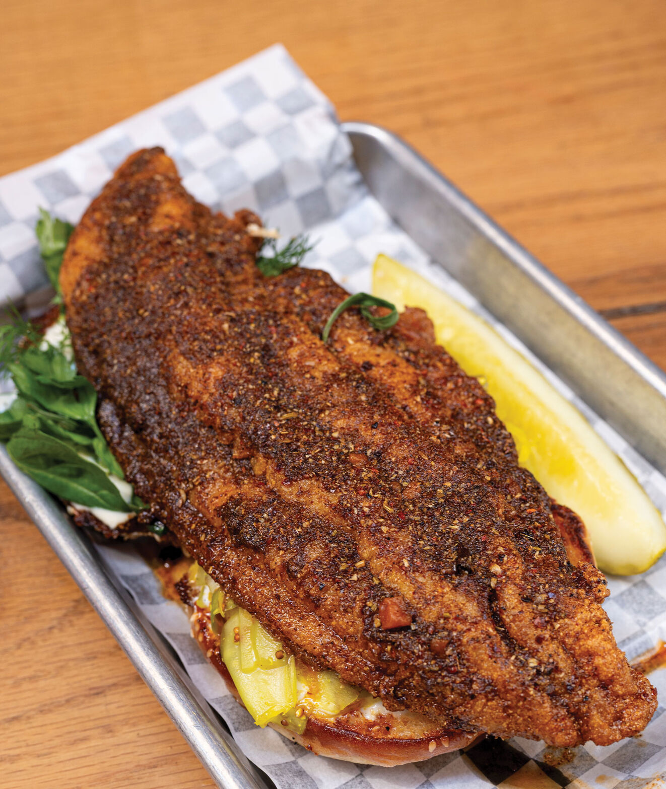 A crispy, well-seasoned fish fillet on top of a bun in a small serving tray
